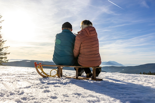 Senior couple relaxing on sled and admiring beautiful mountain view from snowy winter landscape