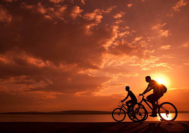 sporty couple Image of sporty couple on bicycles outdoors against yellow or orange sunset. Silhouette. color intensity stock pictures, royalty-free photos & images