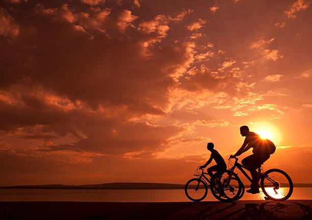 sporty couple Image of sporty couple on bicycles outdoors against yellow or orange sunset. Silhouette. black couple sunset stock pictures, royalty-free photos & images
