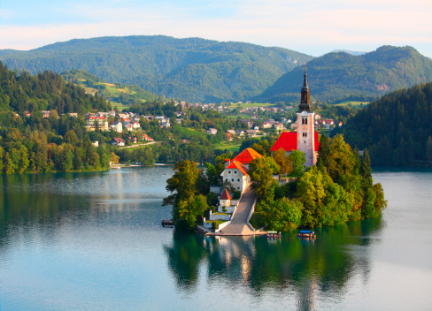 Santa Maria Church catholic church situated on an island on Bled lake with mountains and villages on the background
