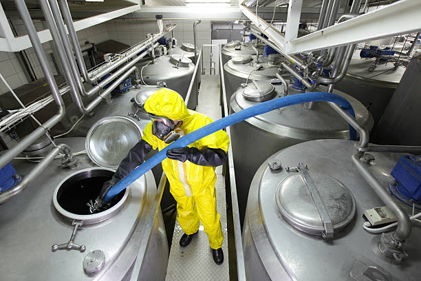 fully protected technician filling large silver tank in factory stock photo