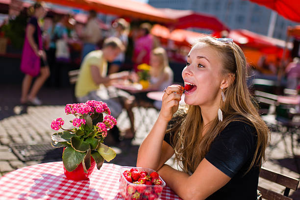 Beautiful girl sits on the market cafe and she eat tasty strawberries