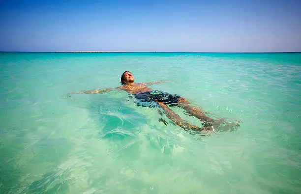 "The man relaxing and sunbathing in sea with green, clear water."