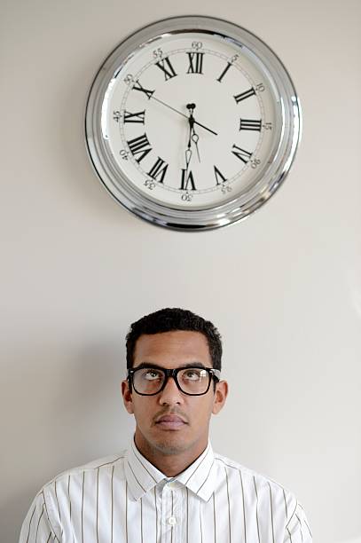 Time concept: young man looking up at wall clock