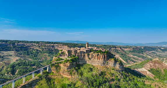 Aerial view of Civita di Bagnoregio Lazio - Italy, Aerial view of the famous town of Civita di Bagnoregio in summer, popular places in italy, world unesco protected places, historical places of the world.\n\nCivita di Bagnoregio is an outlying village of the comune of Bagnoregio in the Province of Viterbo in central Italy. It lies 1 kilometre (0.6 mi) east of the town of Bagnoregio and about 120 kilometres (75 mi) north of Rome. Due to its unstable foundation that often erodes, Civita is famously known as \