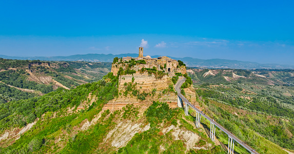 Aerial view of Civita di Bagnoregio Lazio - Italy, Aerial view of the famous town of Civita di Bagnoregio in summer, popular places in italy, world unesco protected places, historical places of the world.\n\nCivita di Bagnoregio is an outlying village of the comune of Bagnoregio in the Province of Viterbo in central Italy. It lies 1 kilometre (0.6 mi) east of the town of Bagnoregio and about 120 kilometres (75 mi) north of Rome. Due to its unstable foundation that often erodes, Civita is famously known as \