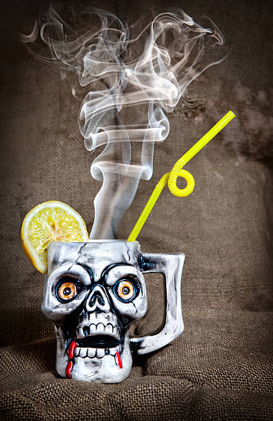 Cocktail in skull mug Skull mug with lemon and yellow stick with steam from inside at textured background on Halloween party gross coffee stock pictures, royalty-free photos & images