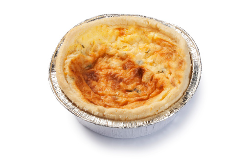 Studio shot of a small individual cheddar and onion quiche in aluminium casing cut out against a white background