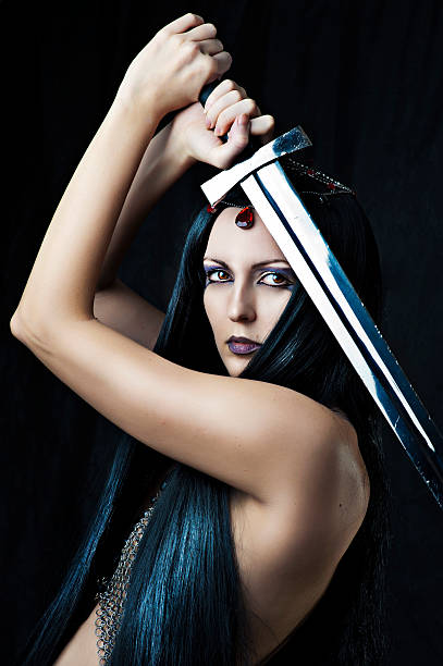 Young sexy woman warrior holding sword in hands with long healthy black hair.