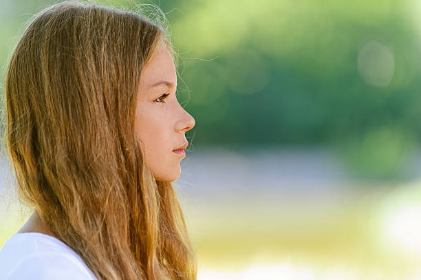 Portrait of beautiful teenage close up profile, against green of summer park.