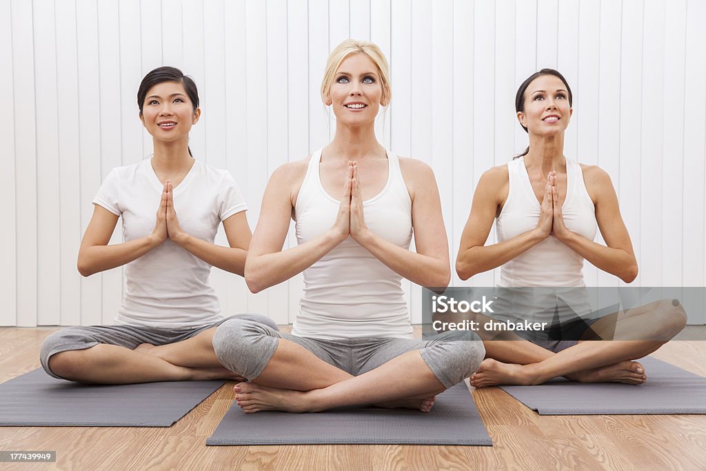 Interracial Group of Three Beautiful Women In Yoga Position An interracial group of three beautiful young women sitting cross legged in a yoga position at a gym Adult Stock Photo