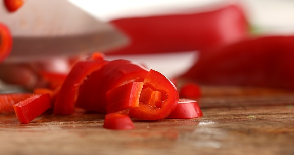 Hands cutting red bell peppers on a wooden chopping board. Woman chopping bell peppers in kitchen close up. Preparing vegetable salad. Healthly food.