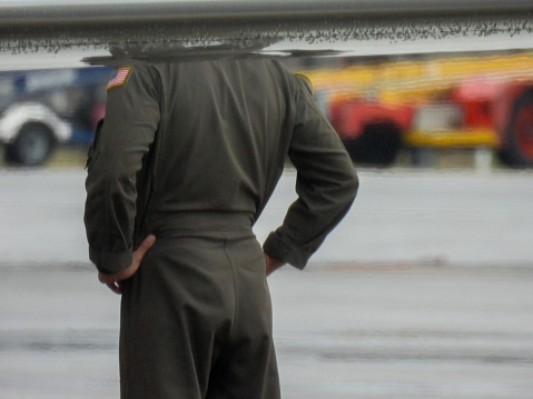 One of the flight crew of a United States Air Force Gulfstream C-37B plane, registration 166377, supervising the refueling after having landed at Sydney Kingsford-Smith Airport from Honolulu.  His head is obscured by the wing.  The crew are members of Fleet Logistics Support Systems One (VR1) and the senior pilot on this flight was a Lt. Commander.  This image was taken through the steel security fence from Ross Smith Avenue, Mascot on an overcast and rainy afternoon on 4 November 2023.
