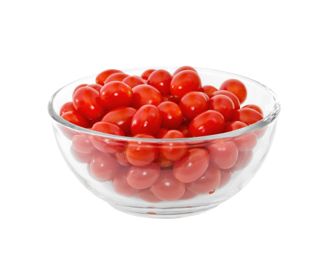 Red cherry tomatoes in glass bowl over white