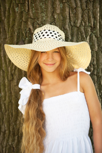 Portrait of smiling beautiful teenage in wide-brimmed hat, against tree trunk.