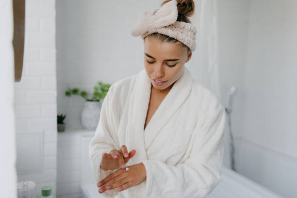 istock Confident young woman in bathrobe applying cosmetic cream on hand while standing in bathroom 1774418928