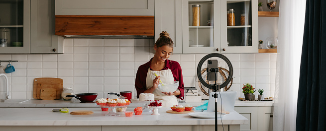 Confident young woman preparing cream for homemade cake and recording video for food blog