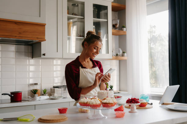 istock Happy young female confectioner using smart phone while making a cake at the domestic kitchen 1774424004