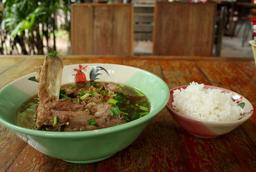 Pork backbone sour and hot soup or Tom leng in traditional ceramic bowl and rice bowl on old brown wood table, Thailand.