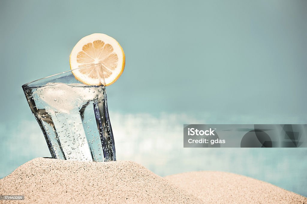 Hot summer day and cold drink on the beach Cold drink with ice and a slice of lemon on the beach on a hot summer day Drinking Glass Stock Photo