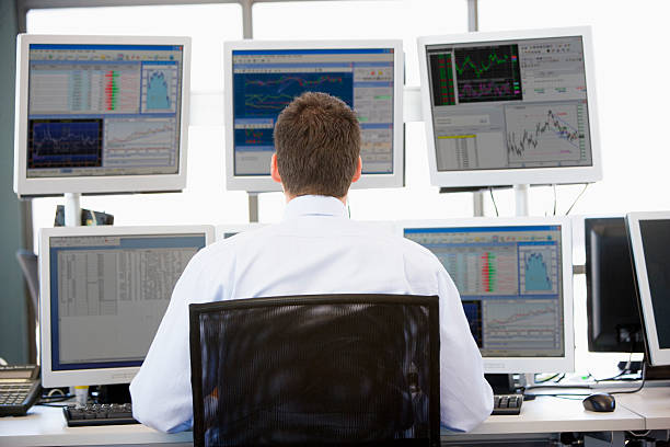 Stock Trader Looking At Multiple Monitors Stock Trader Looking At Multiple Monitors Working In Office dealing room photos stock pictures, royalty-free photos & images