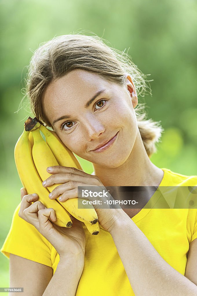 young woman in yellow blouse with banana Portrait of dark-haired smiling beautiful young woman in yellow blouse with banana, against green of summer park. Food Stock Photo