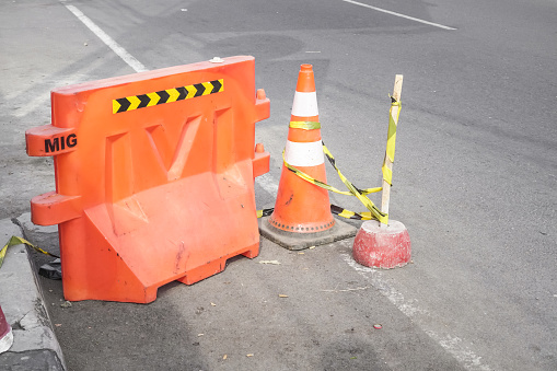 Yogyakarta - August 7, 2023: Road repair renovation. Orange Plastic Barricade safety fence with traffic cone signs on city street indicates the path, road works, detour of a dangerous section of road