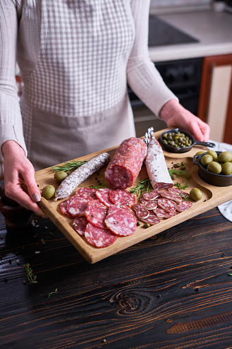 Woman holding wooden cutting board with Traditional Spanish fuet salami sausage at domestic kitchen.