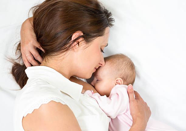 Mother breastfeeding infant daughter while lying down happy mother breast feeding her baby infant suckling stock pictures, royalty-free photos & images