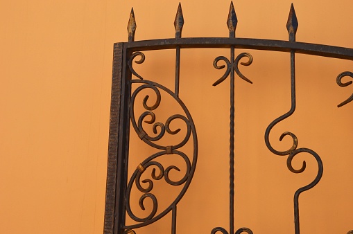 A beautiful forged metal brown fence, a fragment of a gate against the background of a wall.
