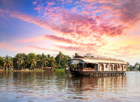 House boat in backwaters near palms at dramatic sunset sky in alappuzha, Kerala, India