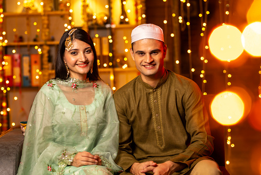 Cheerful young couple looking at camera while sitting in illuminated house during traditional festival