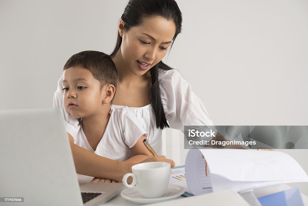 A little boy helping his mom do her homework Mother sitting with her child and working at the same time Asian and Indian Ethnicities Stock Photo