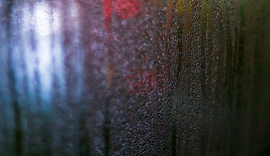 Shot of the window with blurred lights on the background and condensation.