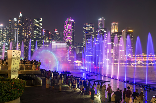 Marina Bay, Singapore - ââOctober 12, 2023: people sightseeing Spectra show of dance fountains, light and water show along promenade by Marina Bay Sands with Central business district modern building.