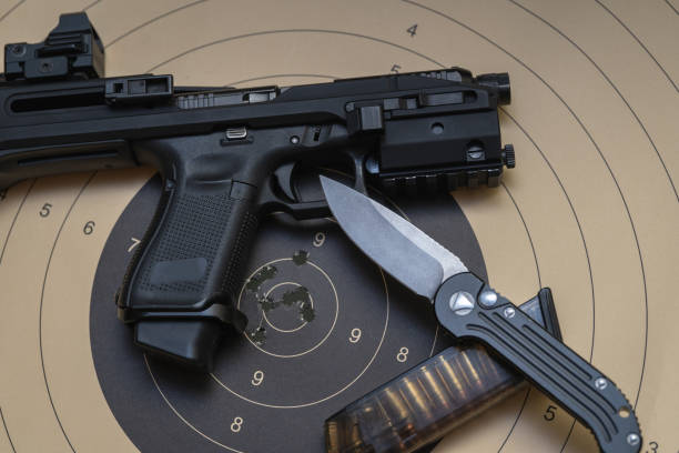 istock Pistol with conversion kit and red dot sight, ammunition magazine with cartridges and tactical folding knife on the paper target with holes from bullet 1774532254