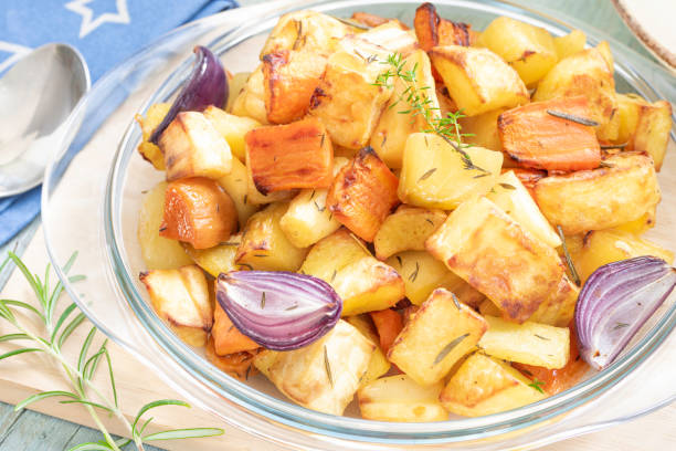 Appetizing homemade oven roasted root vegetables with potatoes, parsnip, beets, carrots, sweet potatoes, red onions, olive oil, thyme leaves and rosemary served in a glass baking dish for a healthy diet
