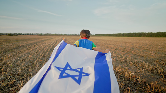 Happy Israeli Jewish little cute boy running with Israel national flag. Independence Day. Patriotism. High quality photo