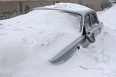 Grey car with a broken rearview mirror under a layer of snow