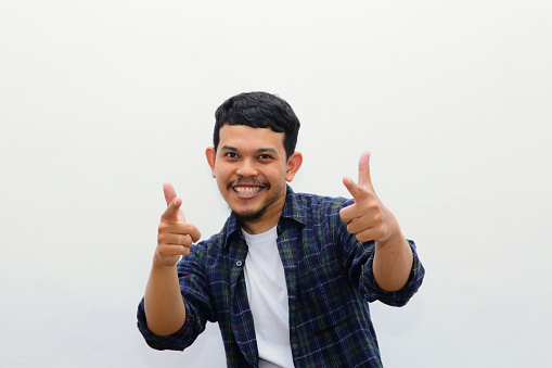 Hey, It's You. Portrait of young asian man in flannel shirt pointing index finger at camera, posing isolated over white background wall. Cheerful smiling guy picking, choosing and indicating