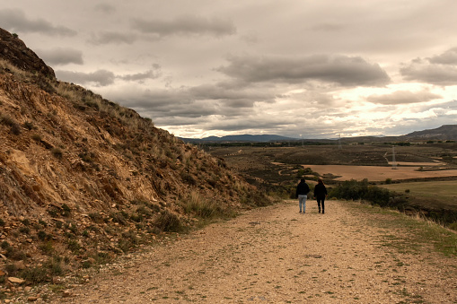 Capture the breathtaking beauty of a serene mountain pathway with two people strolling toward the Bilbilis Roman Ruins in the picturesque town of Calatayud, Zaragoza, Spain. This captivating image is perfect for stock agencies, showcasing nature, history, and exploration.