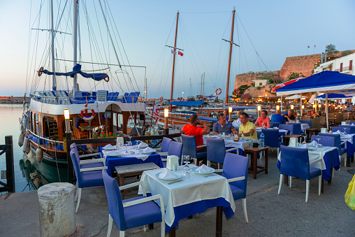 Family sitting seaside on blue chairs and table, typical Greek tavern in Kissamos, Crete, Greece. Traditional setting in a Greek restaurant by the sea.