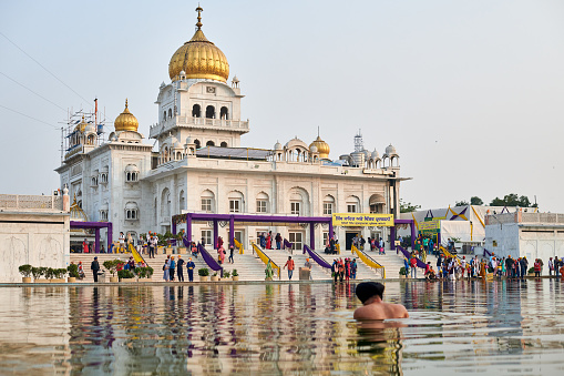 New Delhi, India - 10.11.2022 - Sikh prays in holy pond Sarovar of Gurudwara Bangla Sahib temple in New Delhi, back view of Sikh pilgrim stays in water worships in popular touristic spot in Delhi