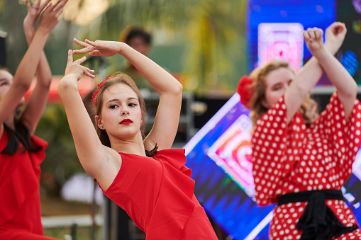 New Delhi, India - 10.12.2022 - Outdoor public park. Young girl in red dress dance on outdoor dancing floor at indian charity christmas fair, attractive female dancer dance makes expressively movements at outdoor stage