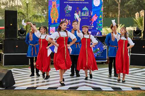 New Delhi, India - 10.12.2022 - Outdoor public park. Teens dance troupe dancing russian folk dance at indian charity christmas fair, group of young girls and boys dancing russian folk dance at outdoor dance floor stage