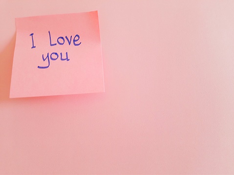 Message written on a pink sticky note, 'I love you', attached to sheet of pink paper with copy space, concept