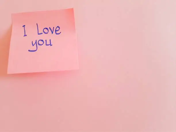 Photo of Message written on a pink sticky note, 'I love you', attached to sheet of pink paper with copy space