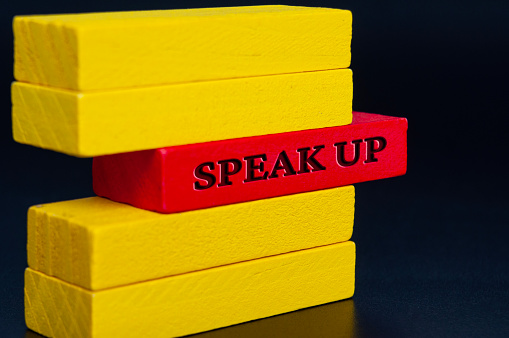 Speak up text on red wooden blocks on dark background.