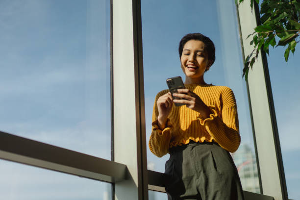 Business People - Portrait of a beautiful Asian Chinese female in yellow cardigan using her phone stock photo