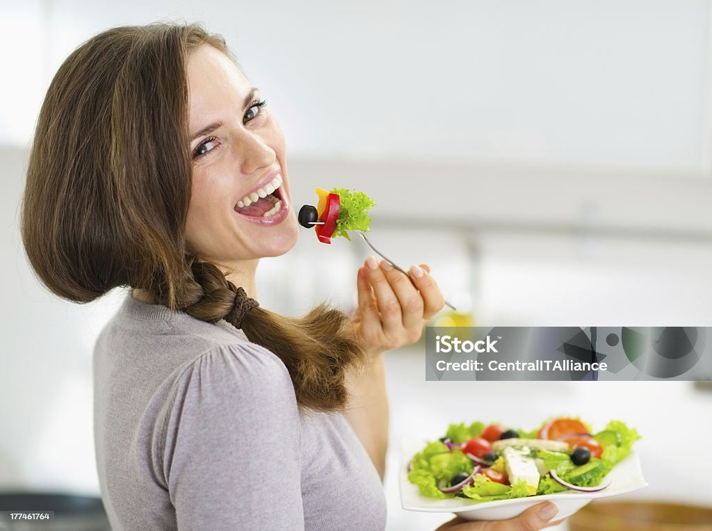 Smiling young woman eating salad in modern kitchen Smiling young woman eating fresh salad in modern kitchen Eating Stock Photo